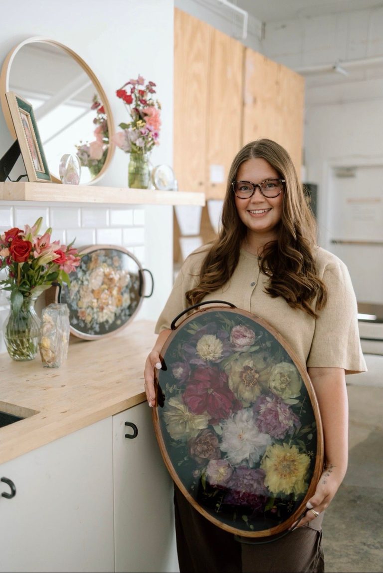 Brand ambassador Caitlyn holding a finished dried flower keepsake next to a Wisedry shadow box display